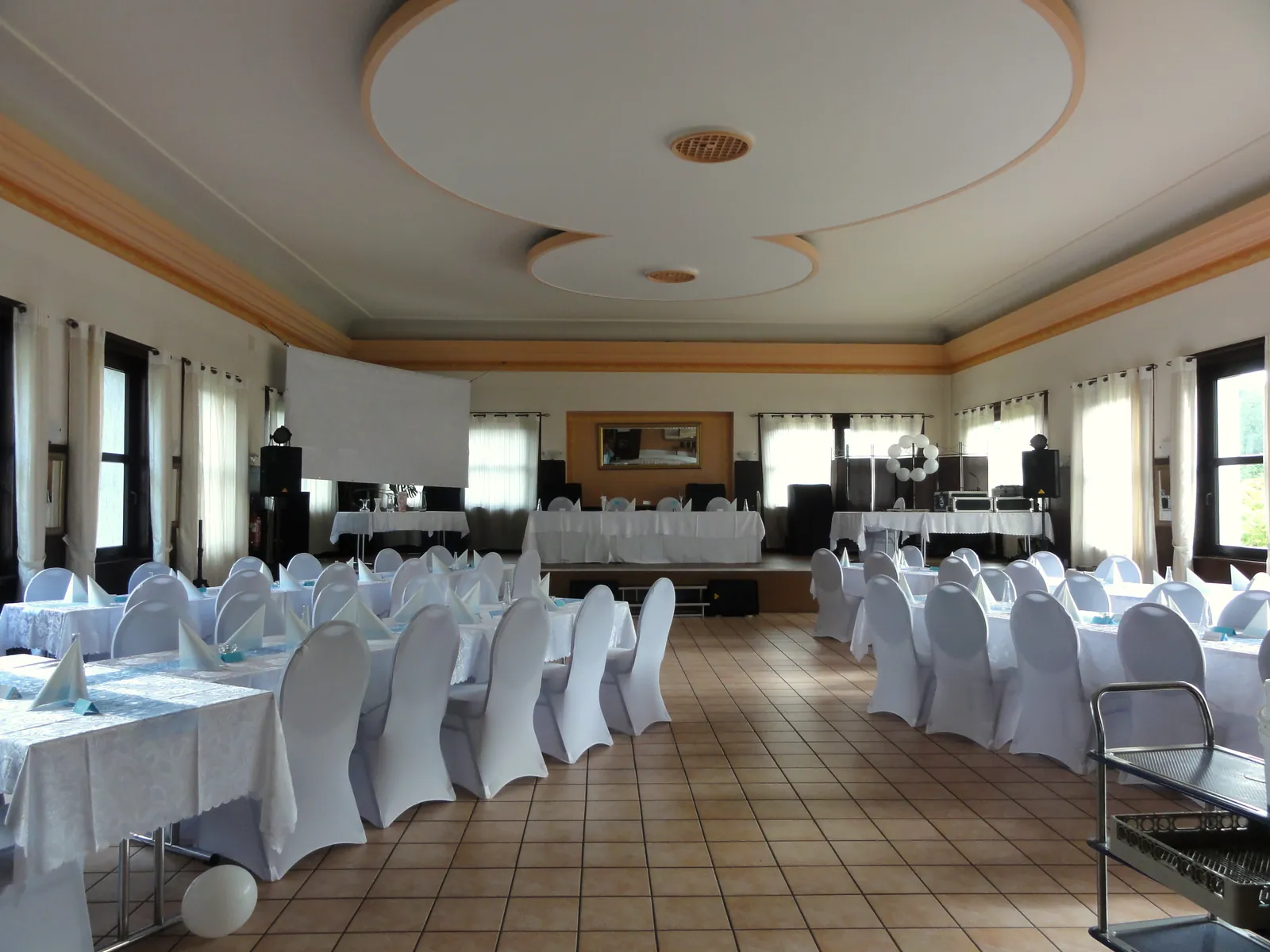 Festive hall with white chair covers, a stage and large windows