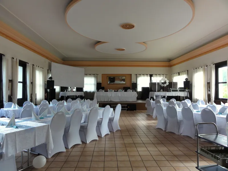 Der Saal mit Bühne, Leinwand und eingedeckten Tischen mit weißen Hussen